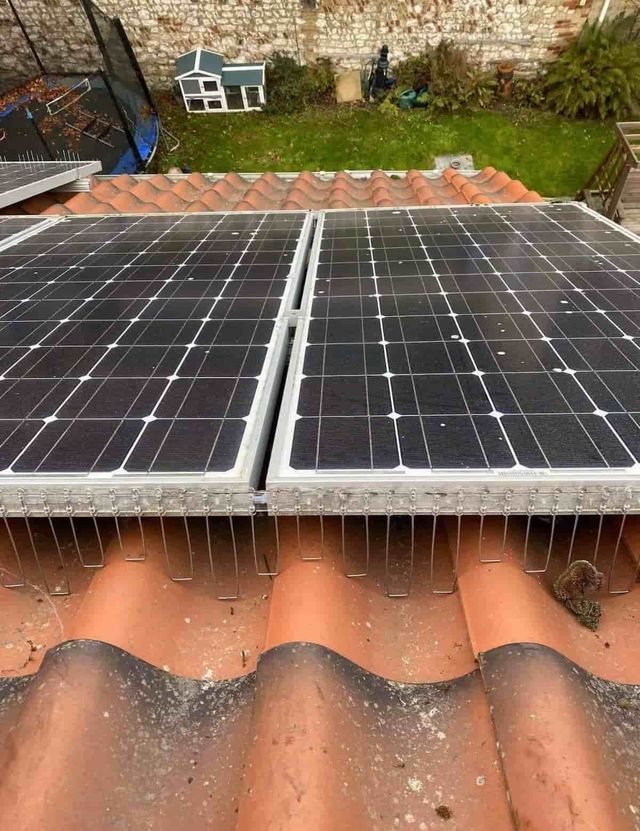 Stainless wire guards fitted along the lower edge of two solar panels on a terracotta pantile roof